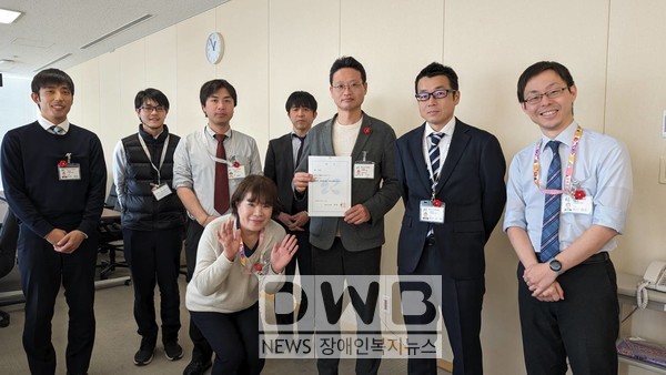 동백꽃 뱃지를 단 기노카와시 지역창생과 직원들과 함께, 가운데 임명장을 들고 있는 서귀포시 직원 강문규 팀장